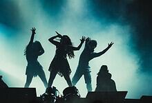 Silhouettes of five performers dancing on stage with blue and green lighting effects.