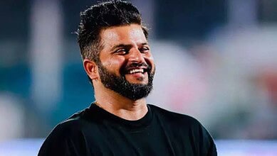 Smiling man with a beard and short hair in a black shirt outdoors.