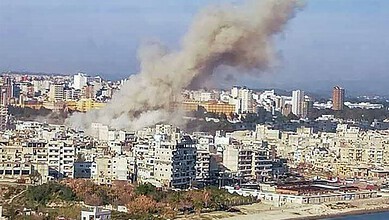 Smoke rises over a city after a devastating ordnance blast in Syria, causing casualties and destruction.