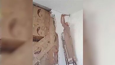 Man breaking wall to reveal a secret library behind it in Syria.