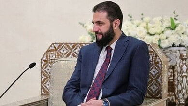 Syrian president with beard in a blue suit during a formal meeting.