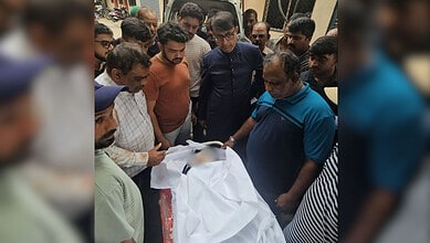 Group of people gathered around a body covered with a white cloth, mourning and paying respects.