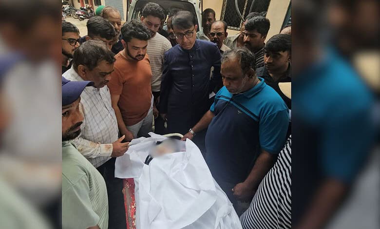 Group of people gathered around a body covered with a white cloth, mourning and paying respects.