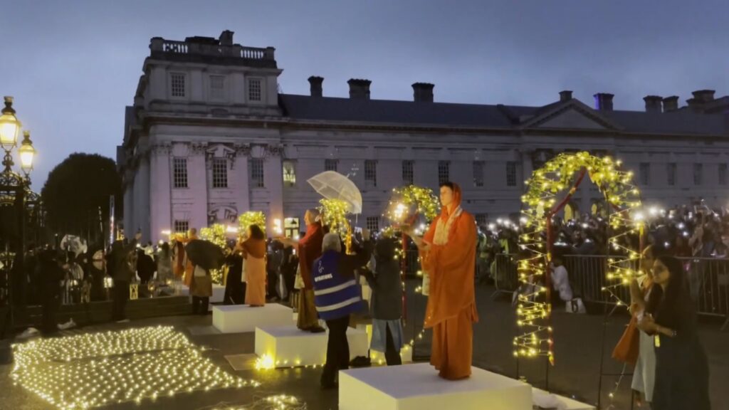 People gather for Ganga Aarti at Thames in London during evening with lights and a priest performing the祭.