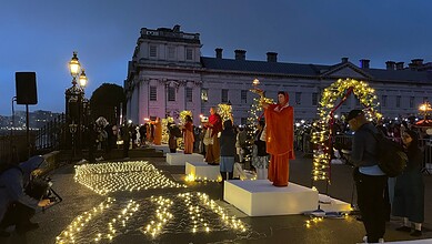 People gathered outdoors during evening with decorative lights and a performer on a stage.