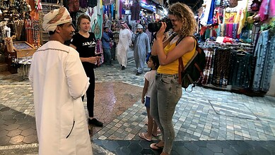 Tourists shopping at a lively market in Oman with colorful textiles and local vendors.