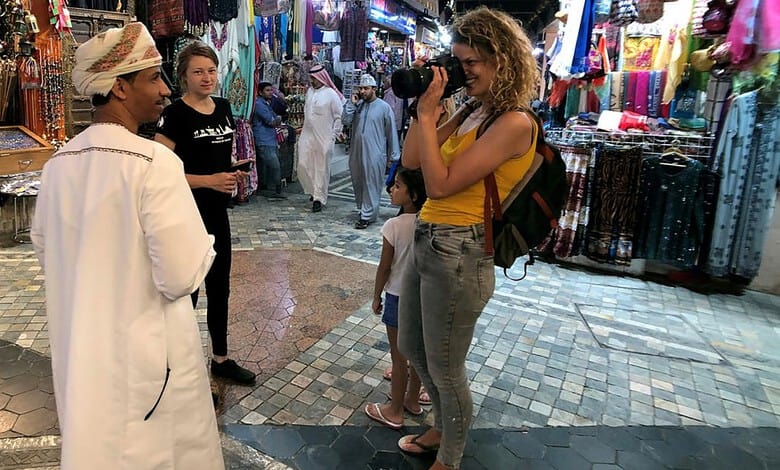 Tourists shopping at a lively market in Oman with colorful textiles and local vendors.