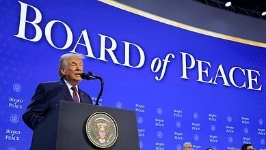 Donald Trump speaking at the Board of Peace event with a blue backdrop and official seal.
