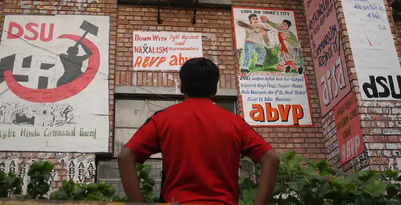 Young man in red shirt looking at political posters on a brick wall.