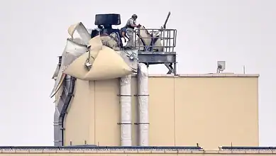 Workers inspect damage on top of a beige industrial building after an apparent attack.