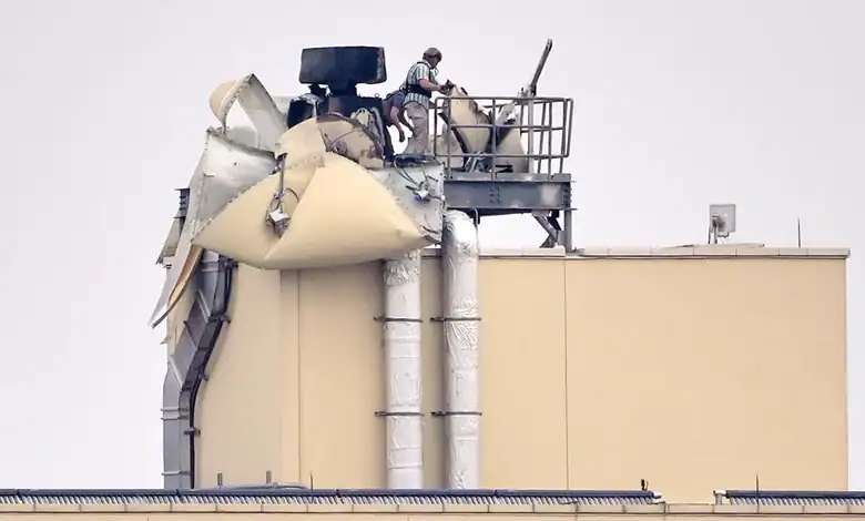 Workers inspect damage on top of a beige industrial building after an apparent attack.