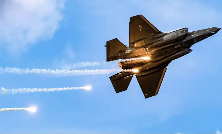 F-35 fighter jet flying at high speed with afterburners on against blue sky.