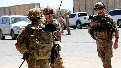 US troops in military gear standing near vehicles in Iraq.