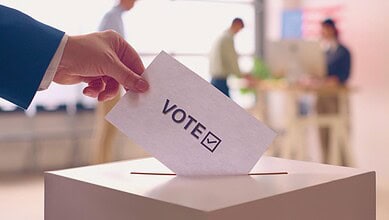 Person casting vote in ballot box at polling station for election process.