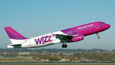 Wizz Air aircraft in pink livery ascending during takeoff at airport.
