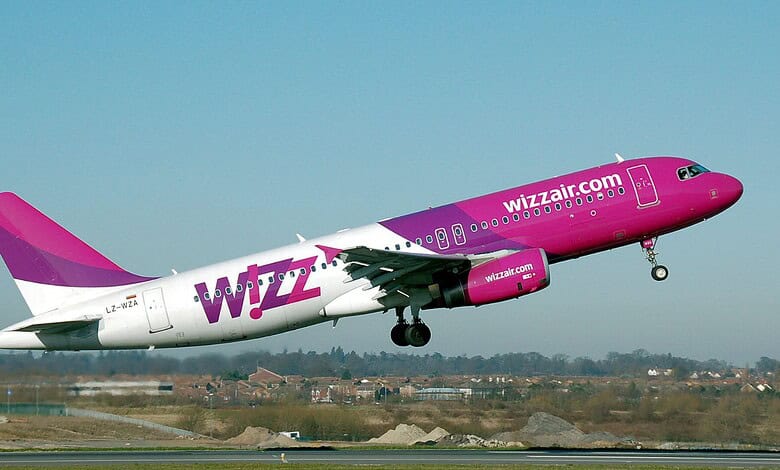 Wizz Air aircraft in pink livery ascending during takeoff at airport.