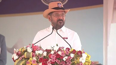 Revanth Reddy speaking at a public event with a floral backdrop.