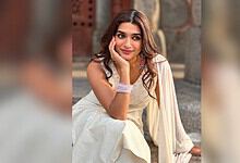 Aafiya Sayed smiling in traditional dress, sitting outdoors with a stone wall background.