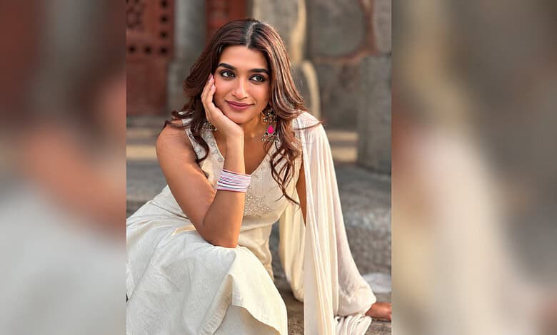 Aafiya Sayed smiling in traditional dress, sitting outdoors with a stone wall background.