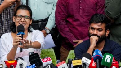 Woman speaking into microphone at press conference with journalists and microphones present.