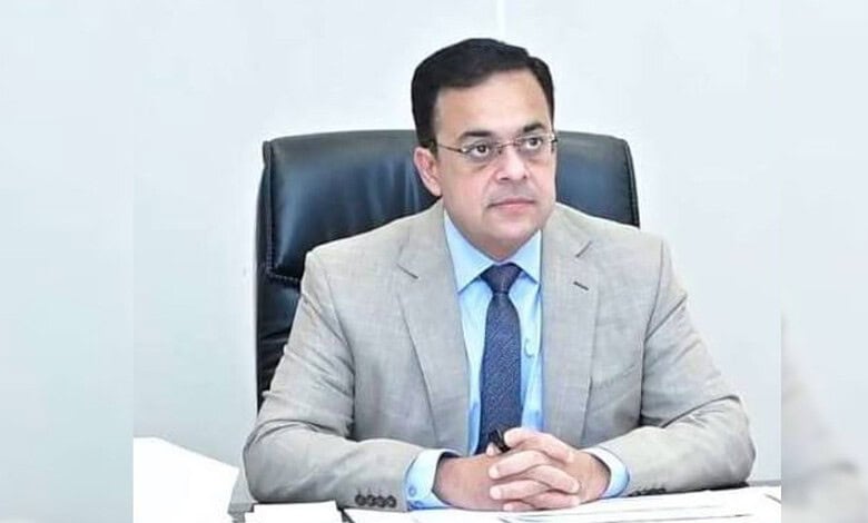 Pakistani official in a grey suit and blue tie sitting at a desk with hands clasped.