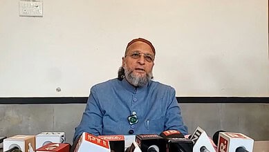 Elderly man in blue kurta speaking at a press conference with microphones.