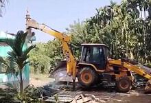 Excavator demolishing structures amidst greenery in Assam.
