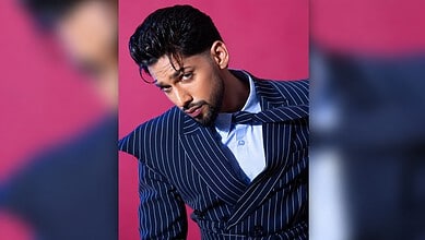 Stylish young man in a pinstripe suit posing against a pink background.