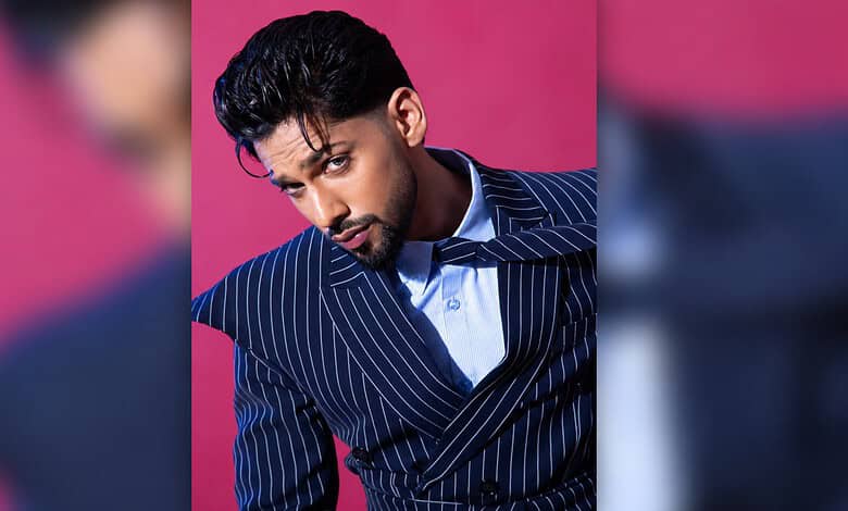 Stylish young man in a pinstripe suit posing against a pink background.