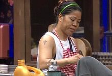 Mary Kom in a kitchen setting, wearing a white apron and red checkered scarf, focused on her task.