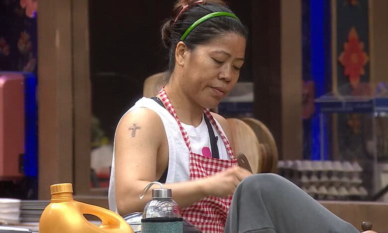 Mary Kom in a kitchen setting, wearing a white apron and red checkered scarf, focused on her task.