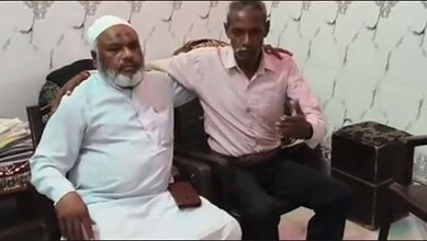 Two men, one elderly Muslim man and a younger man, sitting together in a community setting in Bijnor.