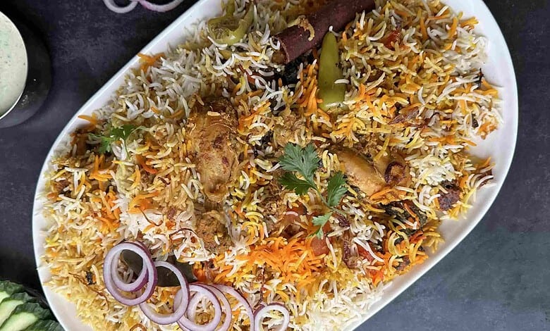 Colourful plate of biryani with chicken, vegetables, and garnishes on a white dish.