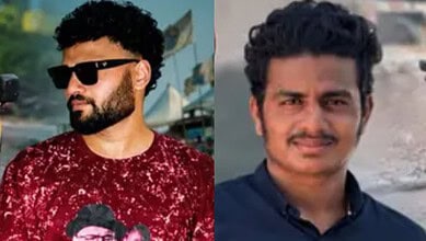 Two men with dark hair and beards, one wearing sunglasses and a red shirt, the other in a dark shirt, in.