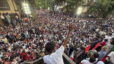 Large crowd gathered at a protest, with a speaker addressing from a vehicle in the foreground.