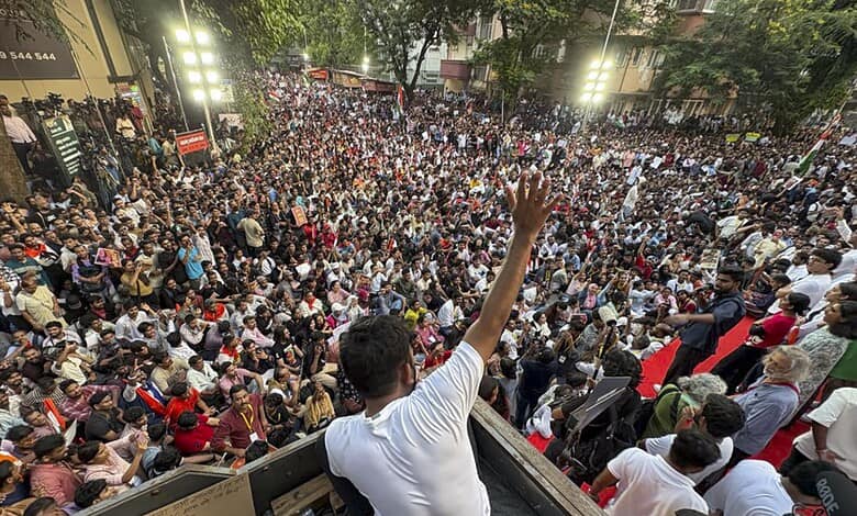 Large crowd gathered at a protest, with a speaker addressing from a vehicle in the foreground.