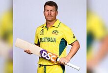 Australian cricket player in yellow uniform holding a cricket bat.