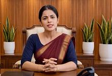 Woman in traditional attire speaking in an office setting with potted plants behind her.