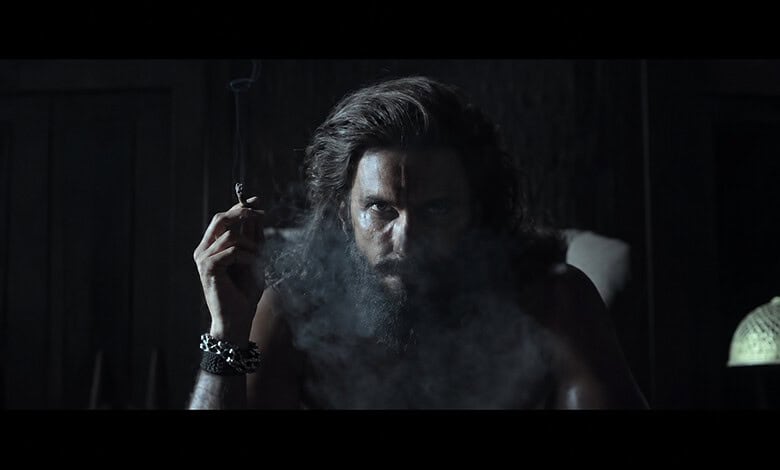 Ranveer Singh as Dhurandhar in a dark scene with smoke and intense expression.
