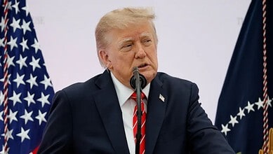 Donald Trump speaking at a press conference with American flags in the background.