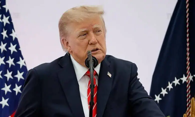 Donald Trump speaking at a press conference with American flags in the background.