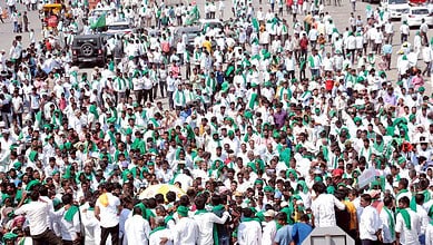 Large crowd of farmers protesting on a highway with banners and umbrellas.