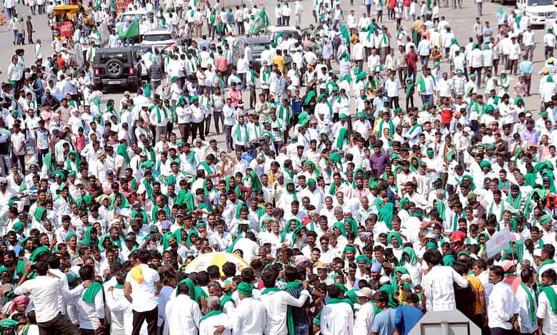 Large crowd of farmers protesting on a highway with banners and umbrellas.