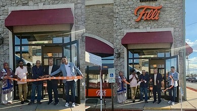 Grand opening of a retail store with people cutting a ribbon outside the store.