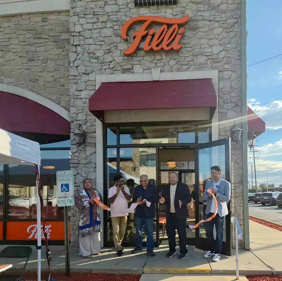 Group of people celebrating outside Filli bakery during grand opening event.