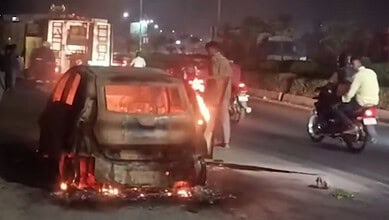Burning car on the roadside near Annojiguda, Ghatkesar, with flames and smoke at night.