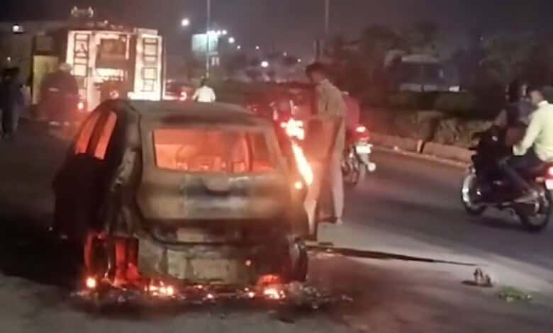 Burning car on the roadside near Annojiguda, Ghatkesar, with flames and smoke at night.