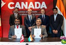 Business leaders from Canada and India sign agreements at a formal event with flags and a 'Canada' banner.