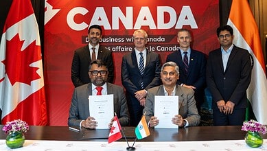Business leaders from Canada and India sign agreements at a formal event with flags and a 'Canada' banner.