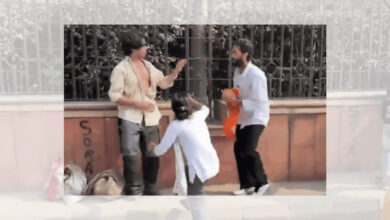 Two men and a woman engaged in a heated argument during a protest in Delhi, with a metal fence in the背景.